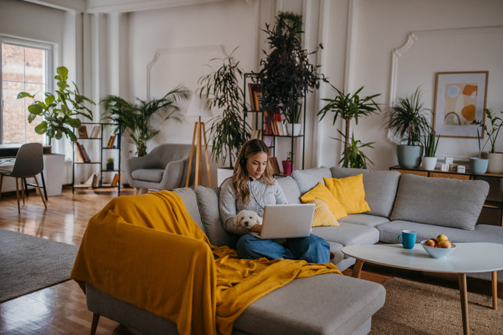 Lady on couch with yellow blanket with indoor plants behind the couch